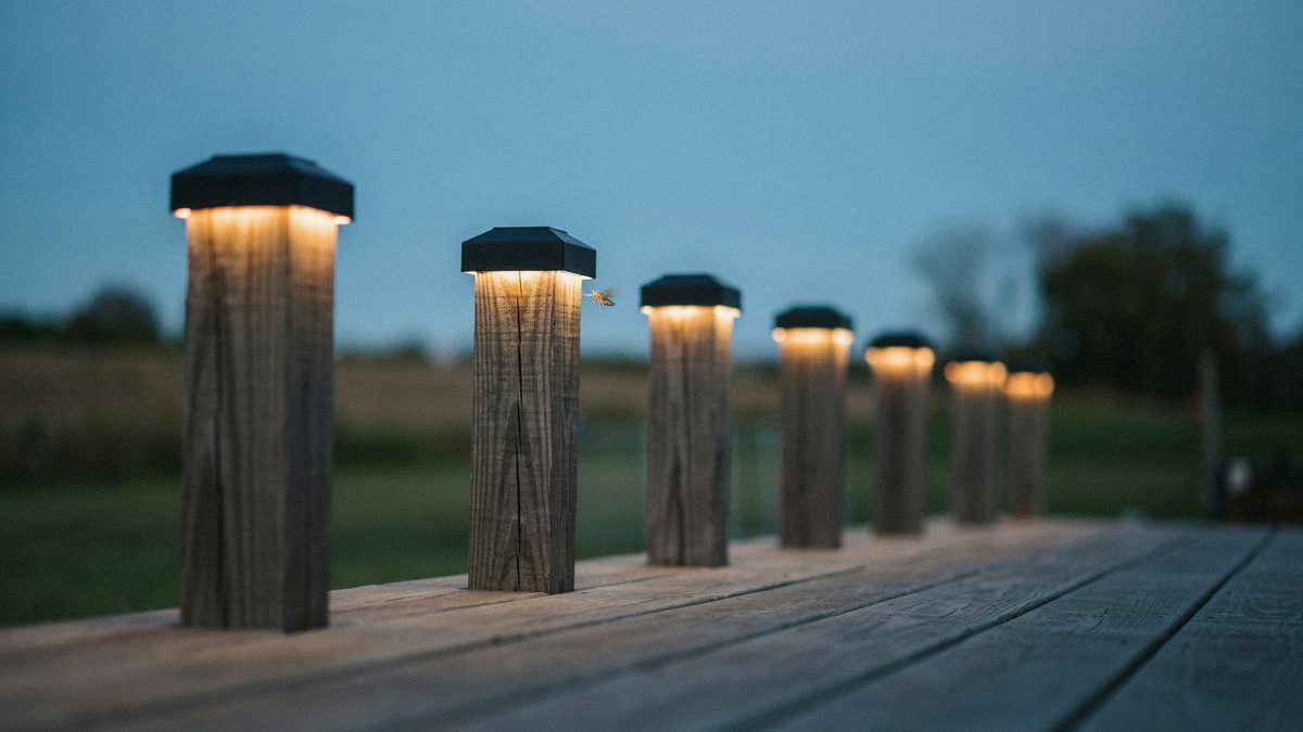 Square black solar cap lights glowing on top of wood deck railing posts