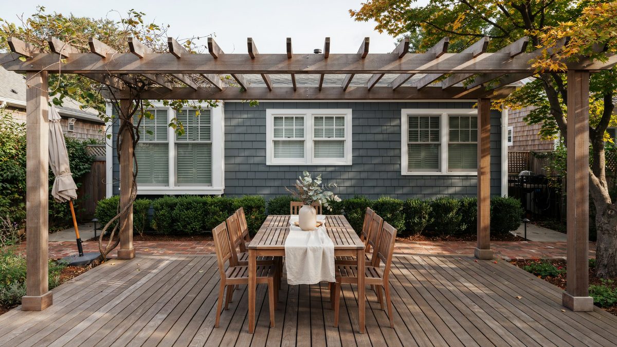 Stained deck with a pergola, dining table and brick tile flooring transition
