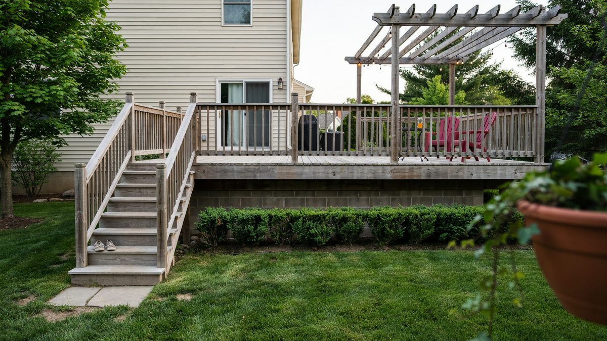 Elevated deck with a pergola over one end, red chairs and stairs to the yard