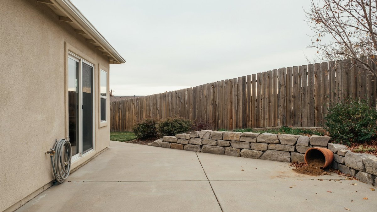 Stone retaining wall and weathered wood fence behind a concrete patio