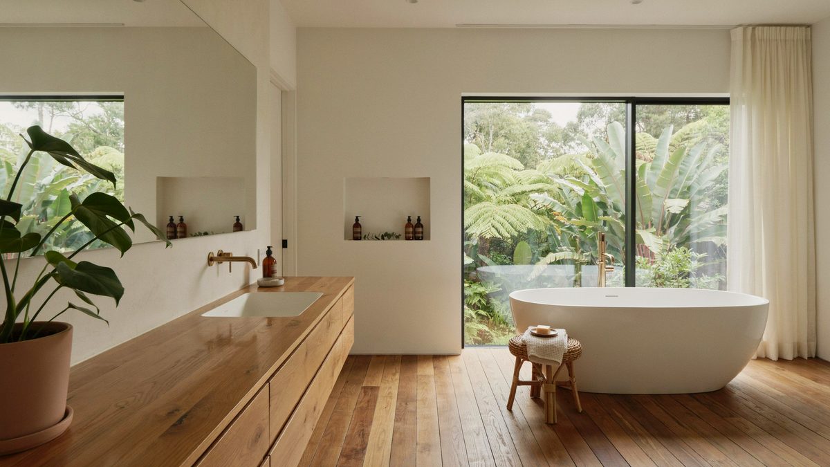 Teak wood vanity counter and plank floor beside a freestanding tub with garden views