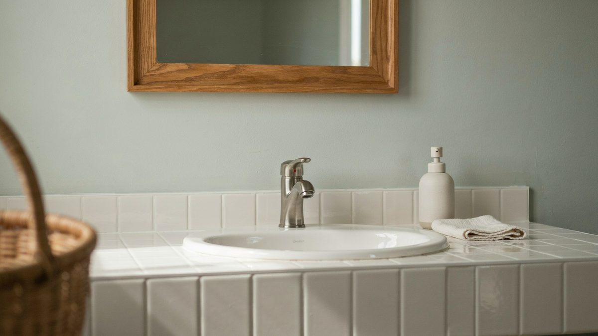 White square ceramic tile countertop surrounding a drop in sink under a wood mirror