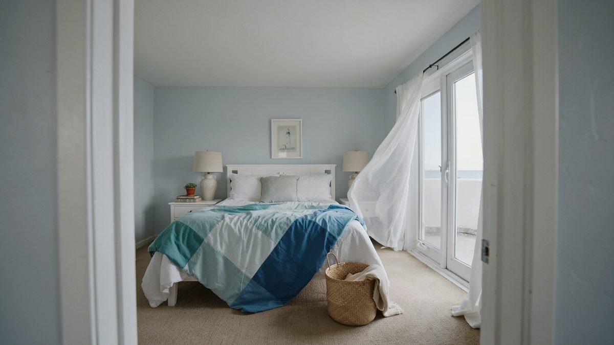 Pale blue coastal room with a teal bedspread and open balcony doors