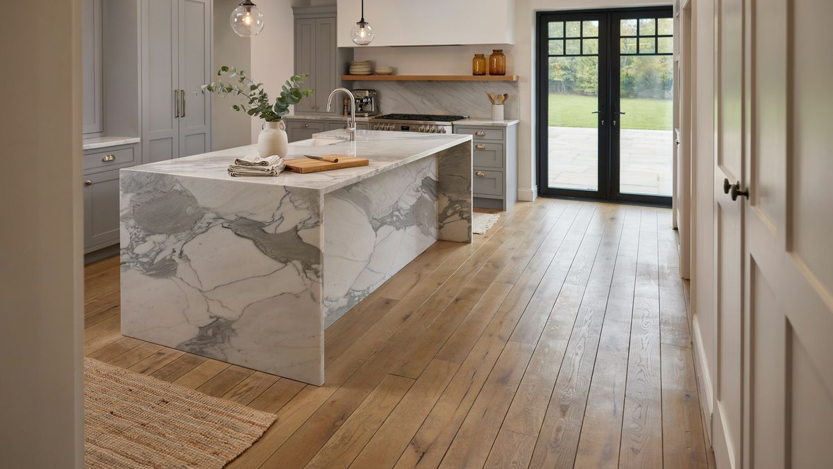 Gray cabinets and a thick marble island facing black French doors to the lawn