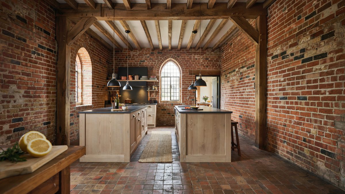 Exposed brick kitchen with timber ceiling beams and two light oak island counters
