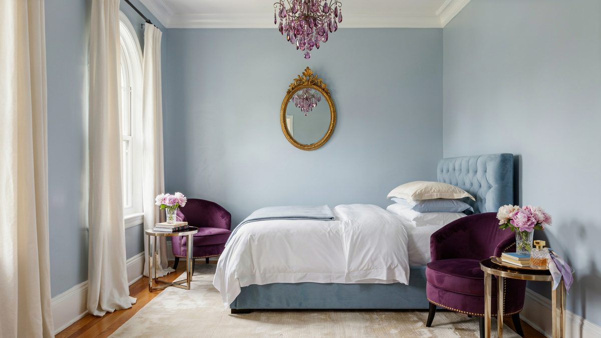 Powder blue walls with a tufted headboard, purple chairs and crystal chandelier