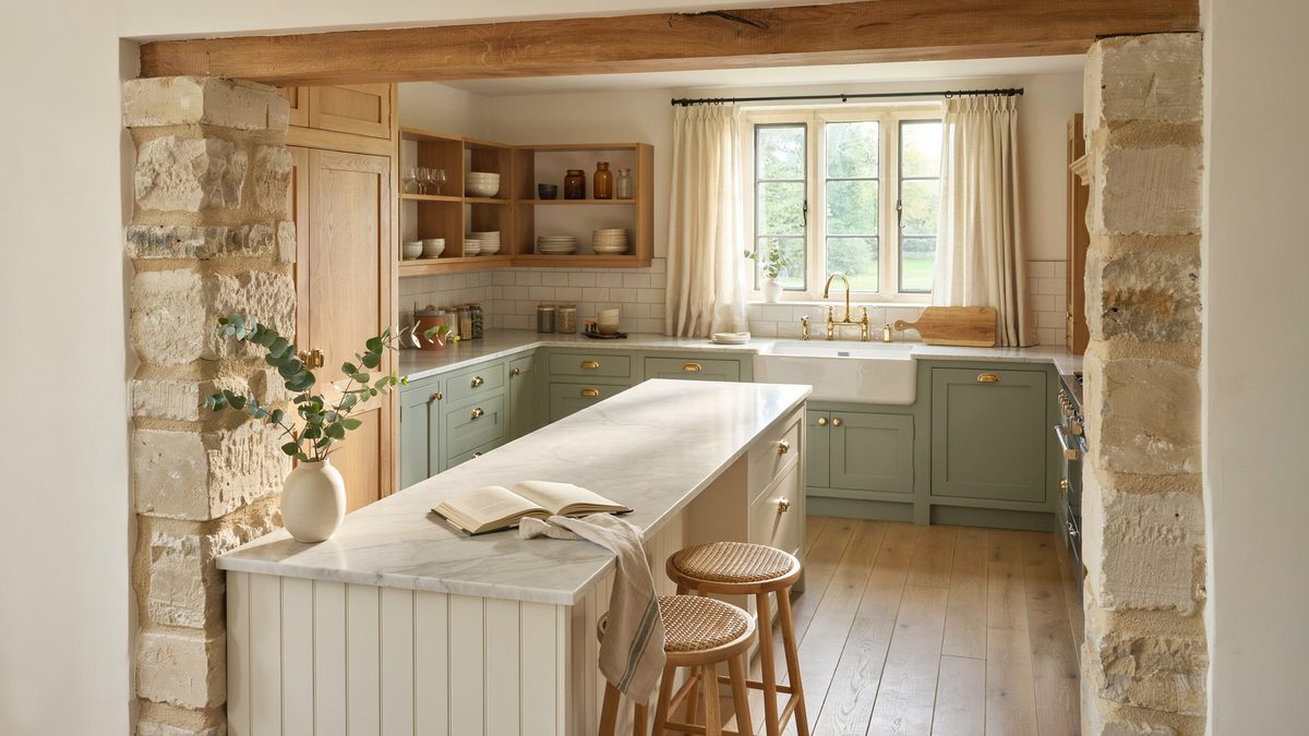 Stone pillars framing a sage green kitchen with a marble island and woven stools