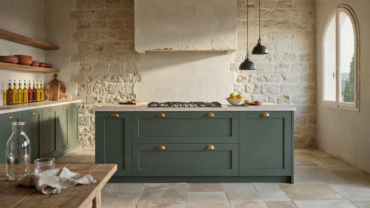 Olive island cooktop set beneath a plaster hood and rough limestone wall