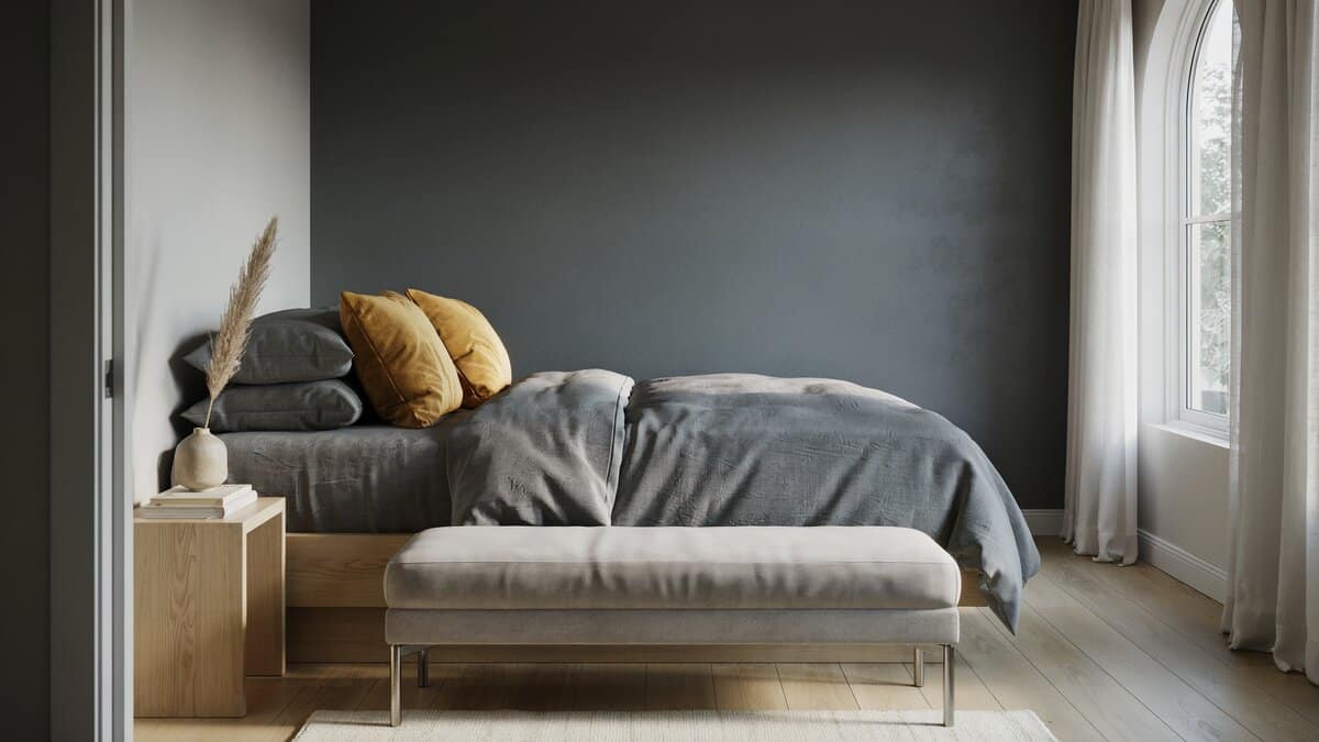 Silver satin bench faces a charcoal accent wall stacked with yellow throw pillows