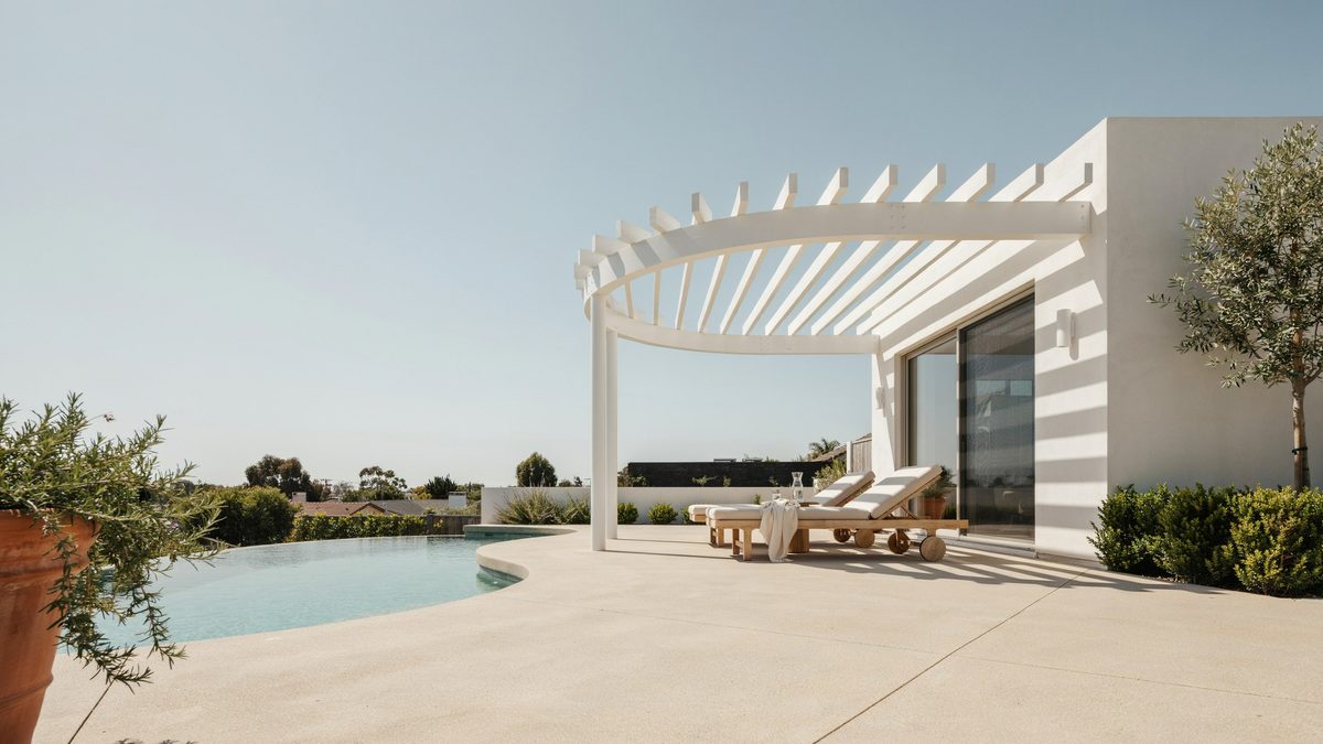 White curved top pergola beside a freeform pool with cushioned sun loungers