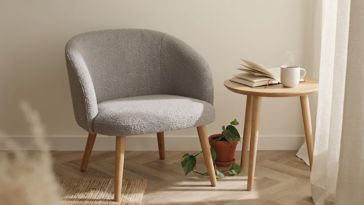 Gray boucle slipper chair with curved arms next to a round side table