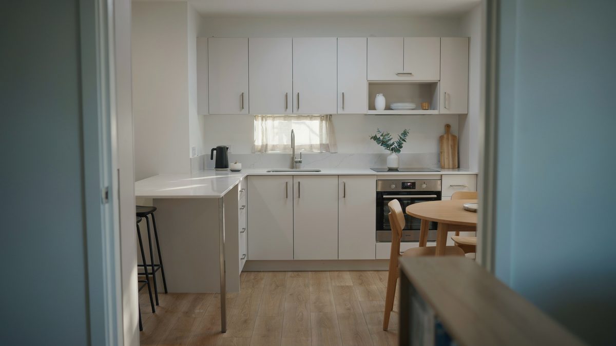 Compact white cabinets wrap a corner with a raised bar counter and teal wall
