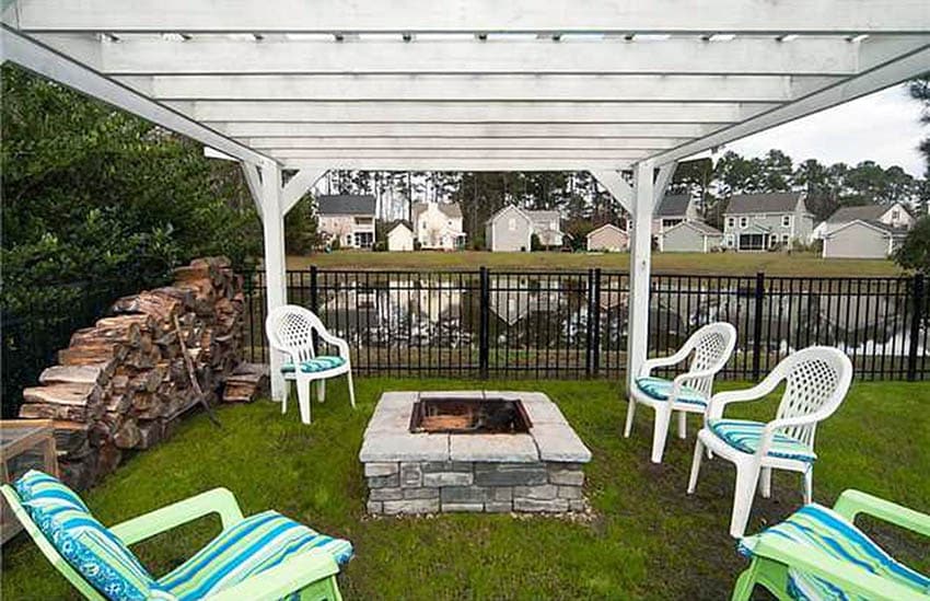 Stacked stone fire pit with white pergola above on grass