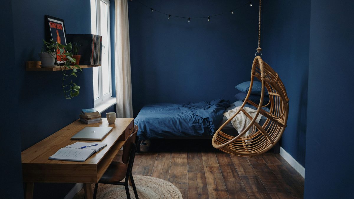 Dark blue teen room with a hanging rattan chair and wood writing desk