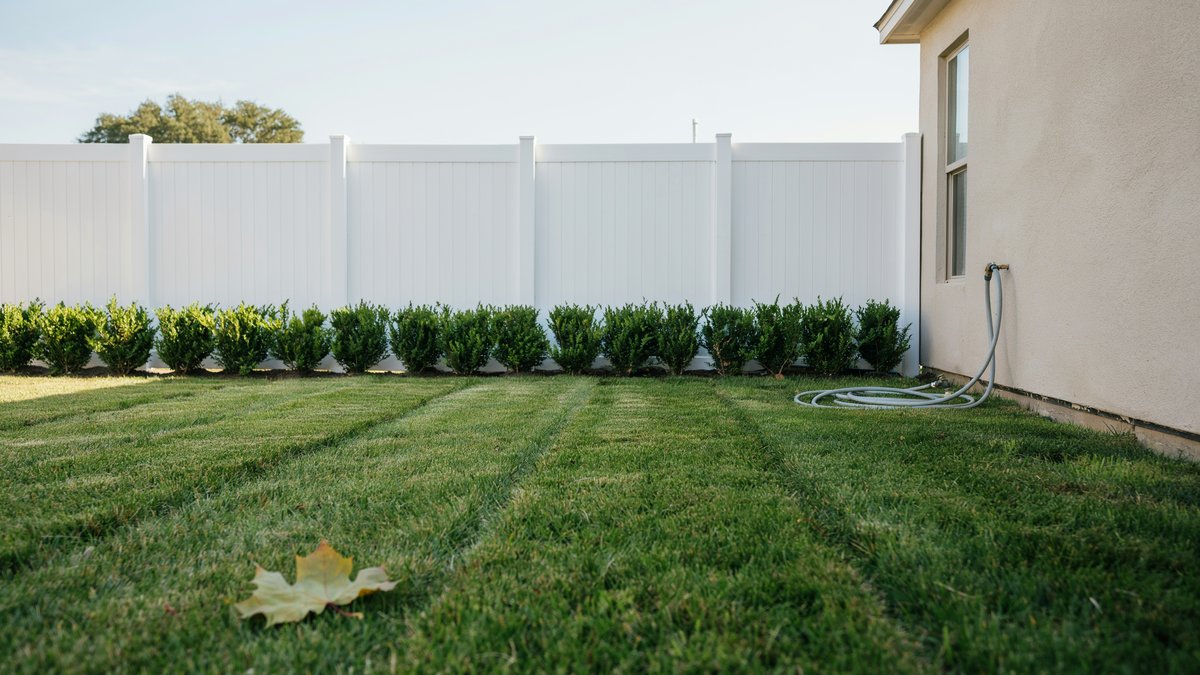 Solid white vinyl fence panels lining a green backyard lawn