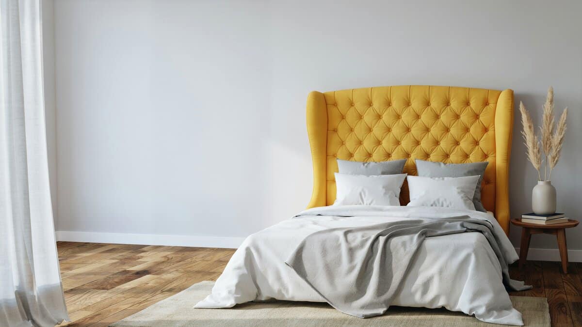 Tall yellow tufted wingback headboard rises behind crisp white and gray bedding