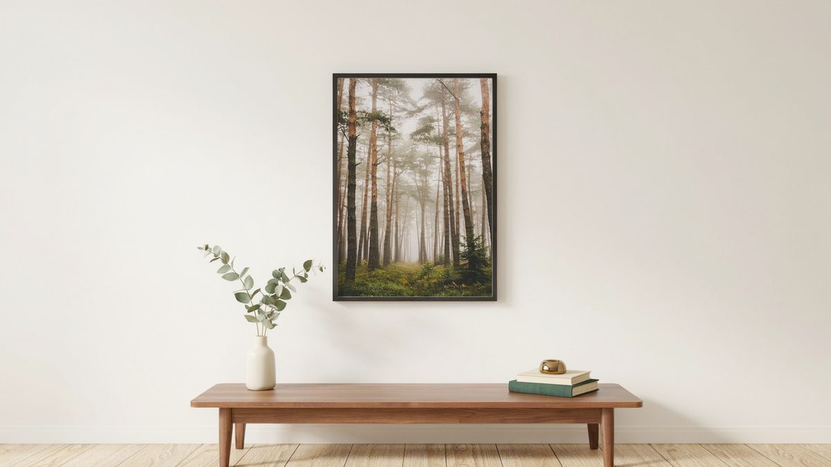 Framed misty forest print above a low wood bench with eucalyptus stems