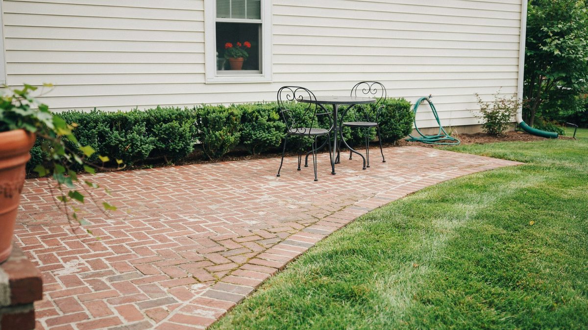 Red brick patio with black wrought iron table beside white clapboard house