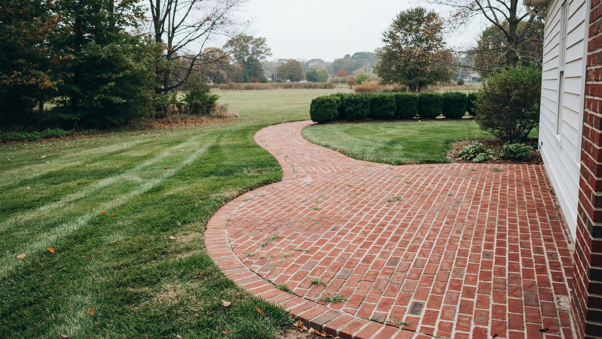 Curved red brick walkway edging a mowed lawn beside a brick home