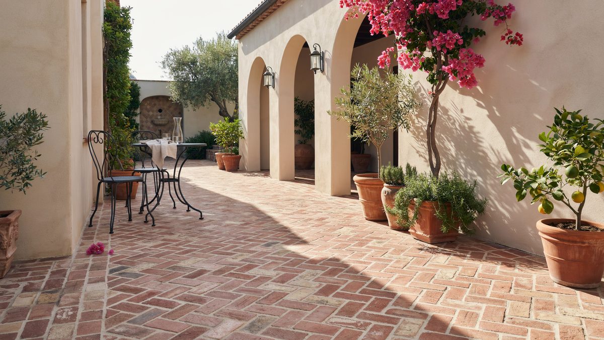 Herringbone brick courtyard with arched stucco loggia and potted olive trees