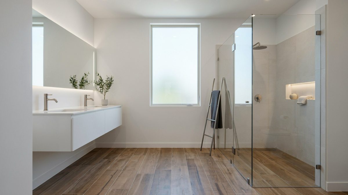 Wood grain plank tile floor beside a frameless glass shower and floating vanity