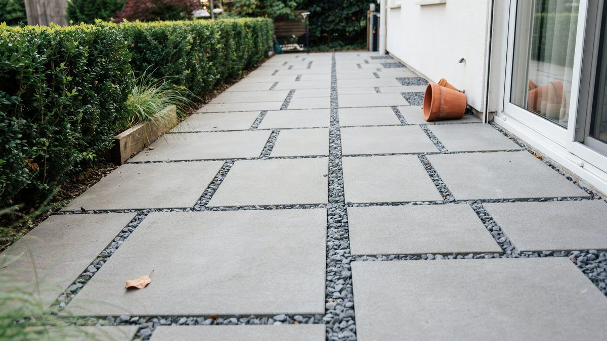 Poured concrete slabs separated by dark gravel strips along a clipped hedge