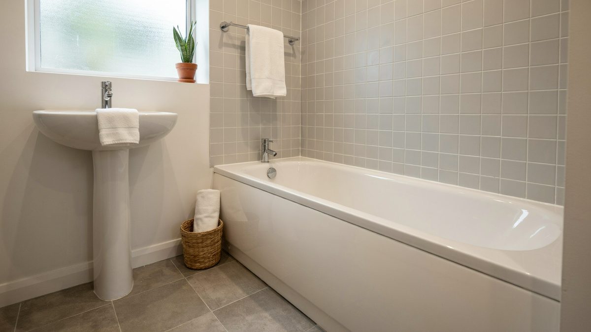 Pale linoleum floor with an alcove bathtub, pedestal sink and tiled walls