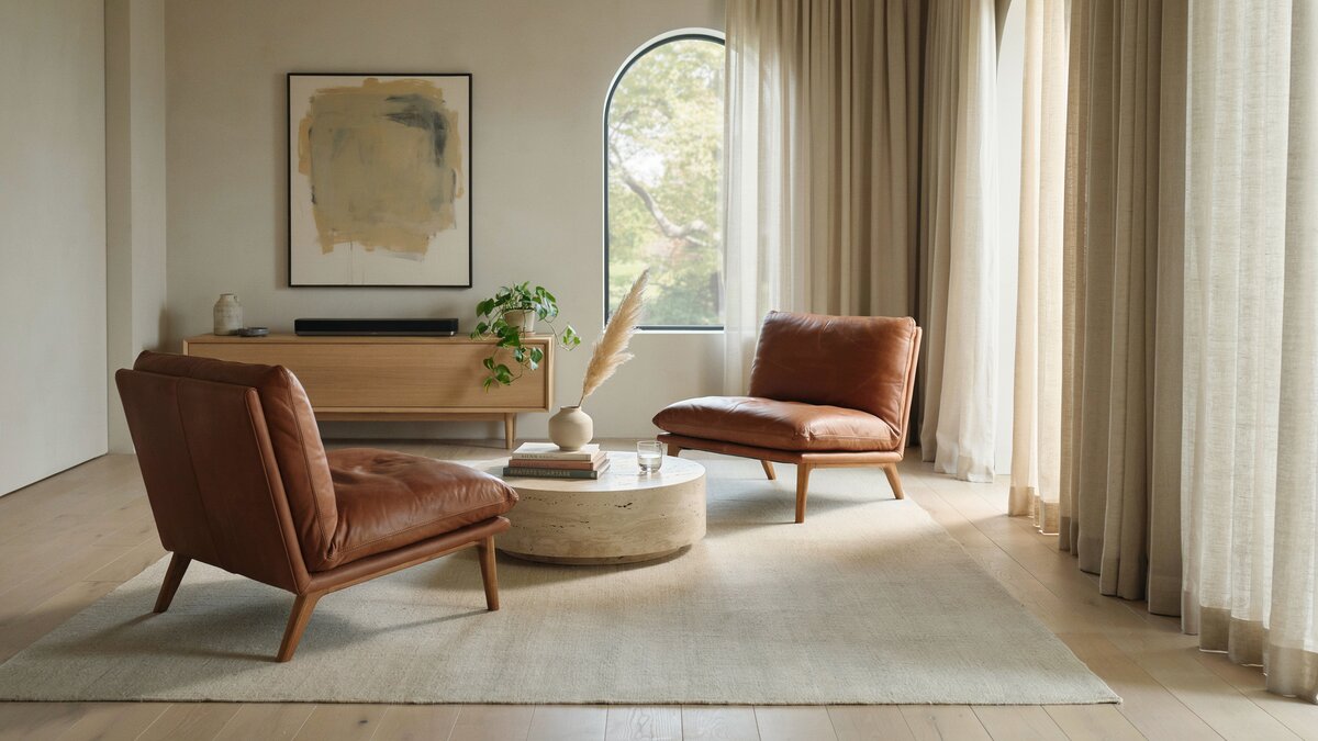 Two tan leather armchairs with a round stone table near an arched window