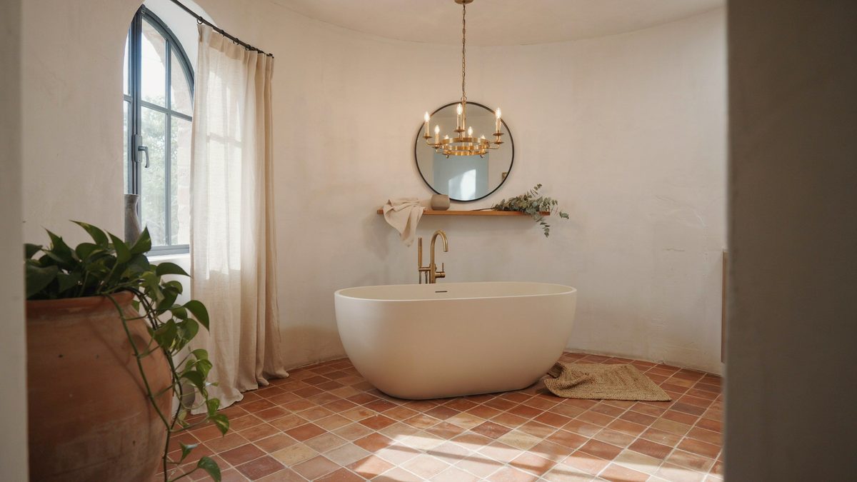 Square terracotta floor tiles under a freestanding tub with a brass chandelier above
