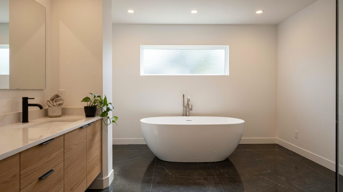 Black granite floor with an oak vanity, white counters and freestanding tub