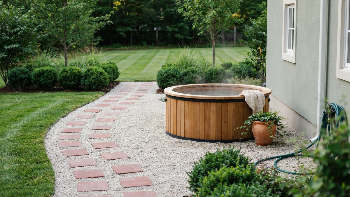 Red paver steps in pea gravel leading to a round cedar hot tub