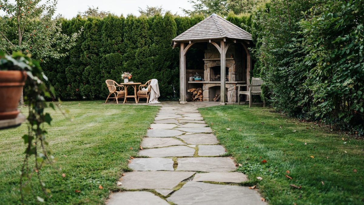 Flagstone path across lawn to a shingled gazebo with a stone fireplace