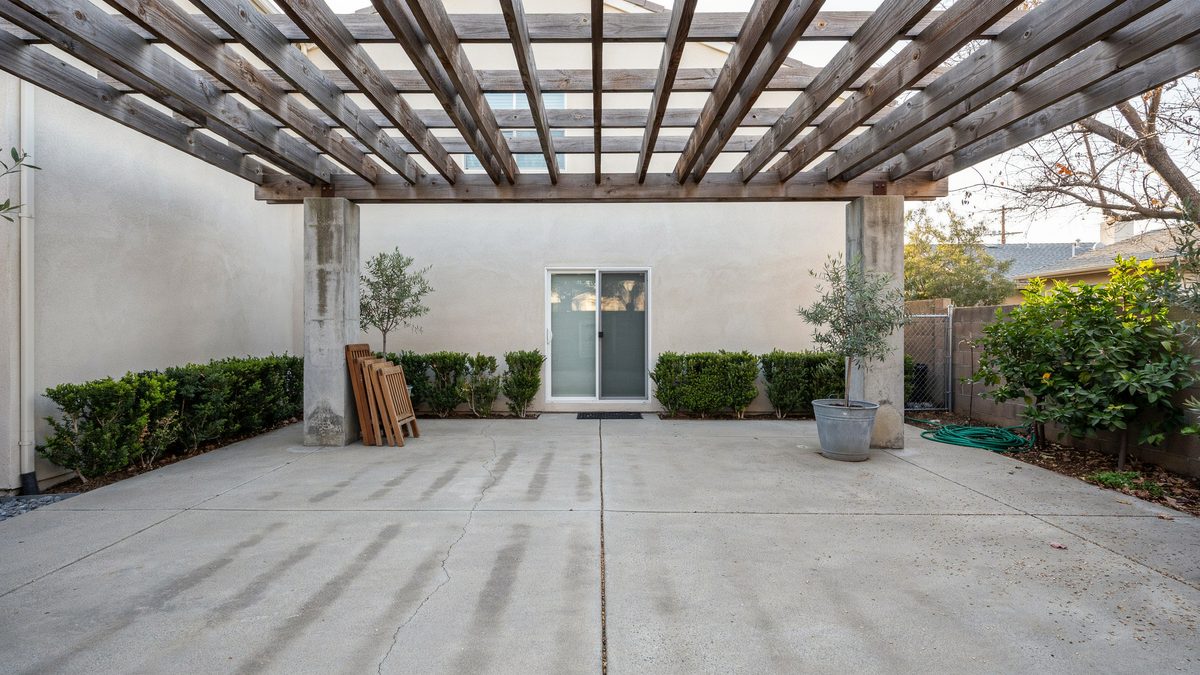 Weathered wood pergola on cement pillars above a wide concrete patio