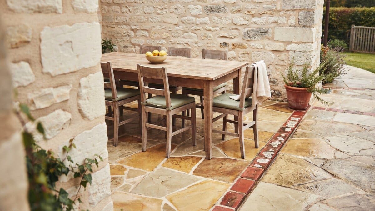 Warm toned stone paving with a brick accent border and weathered wood dining set