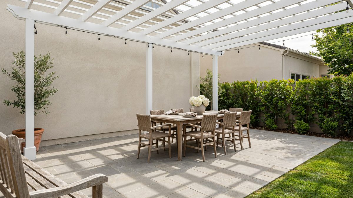 White slatted pergola shading a long outdoor dining table on concrete