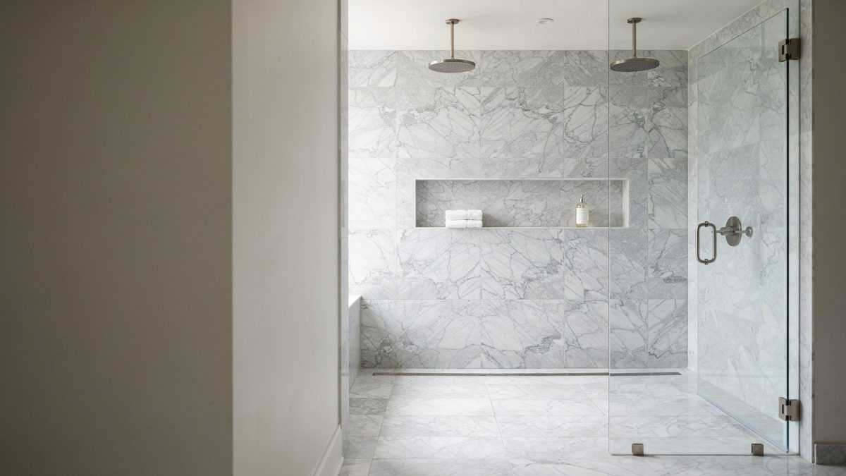 Doorless walk in shower with white marble floors, twin rainfall heads and long niche