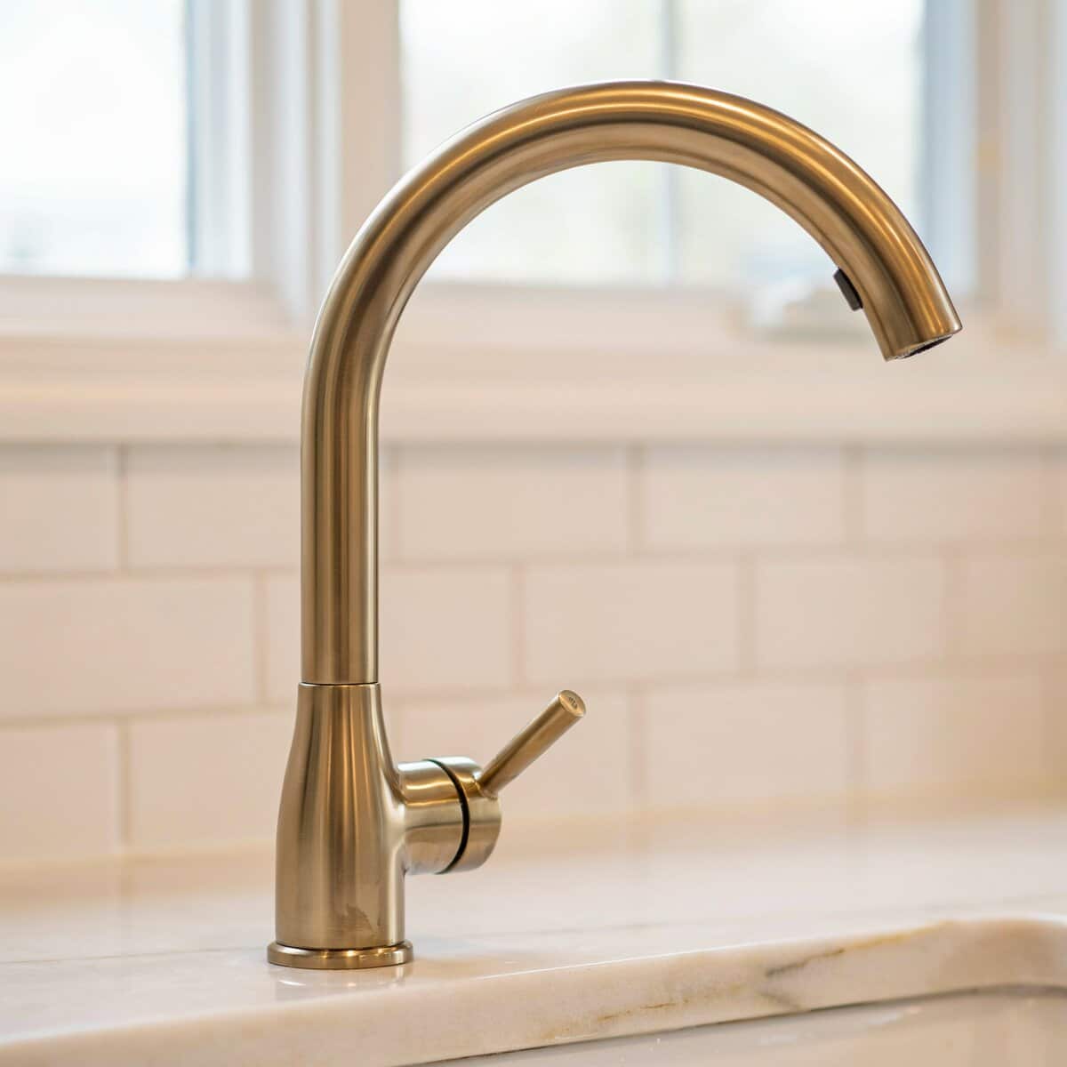 Warm brass gooseneck faucet with single handle on marble countertop