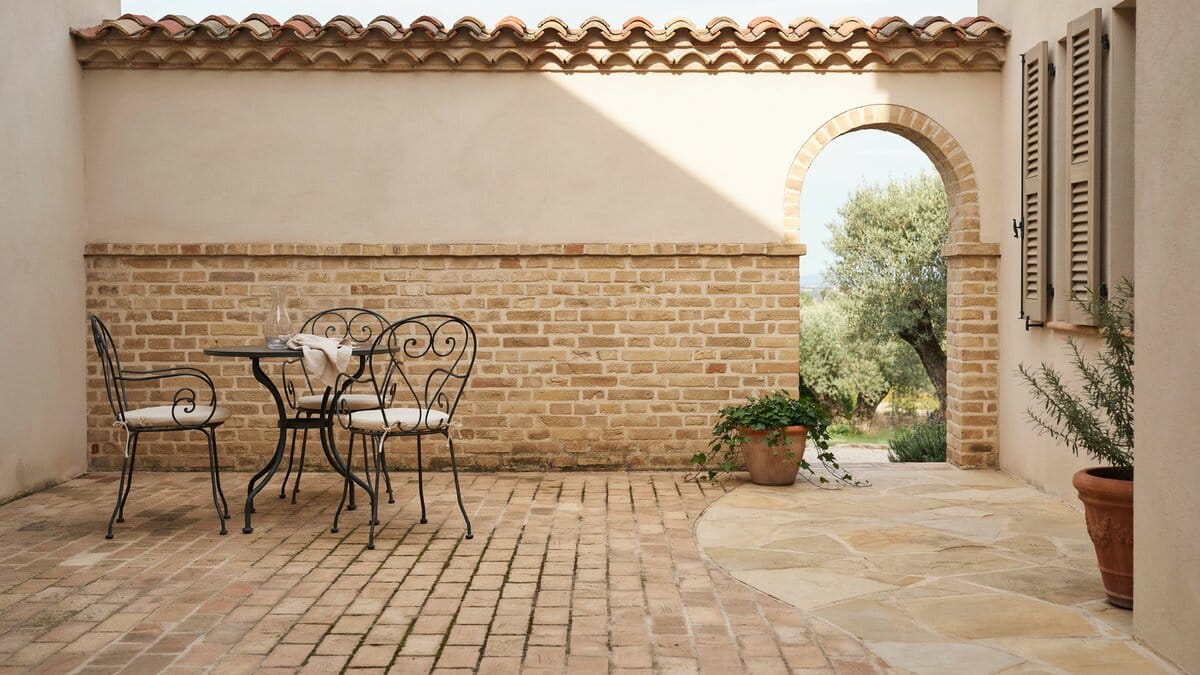 Covered patio pairing tan brick paving with stone and an arched brick wall