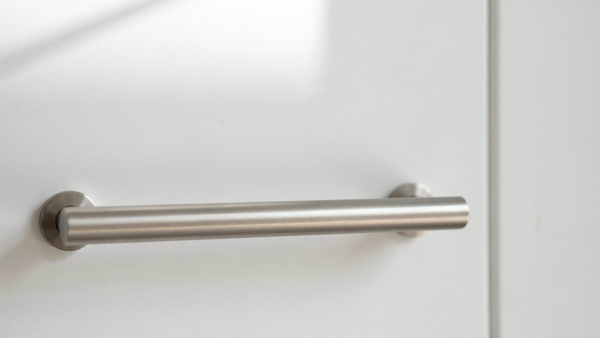 Brushed nickel bar handle mounted on a smooth white cabinet door