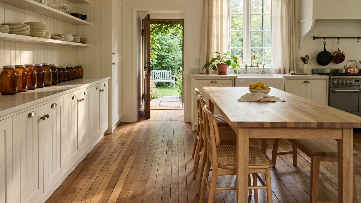 Cream beadboard cabinets line a cottage kitchen with a long wood dining table