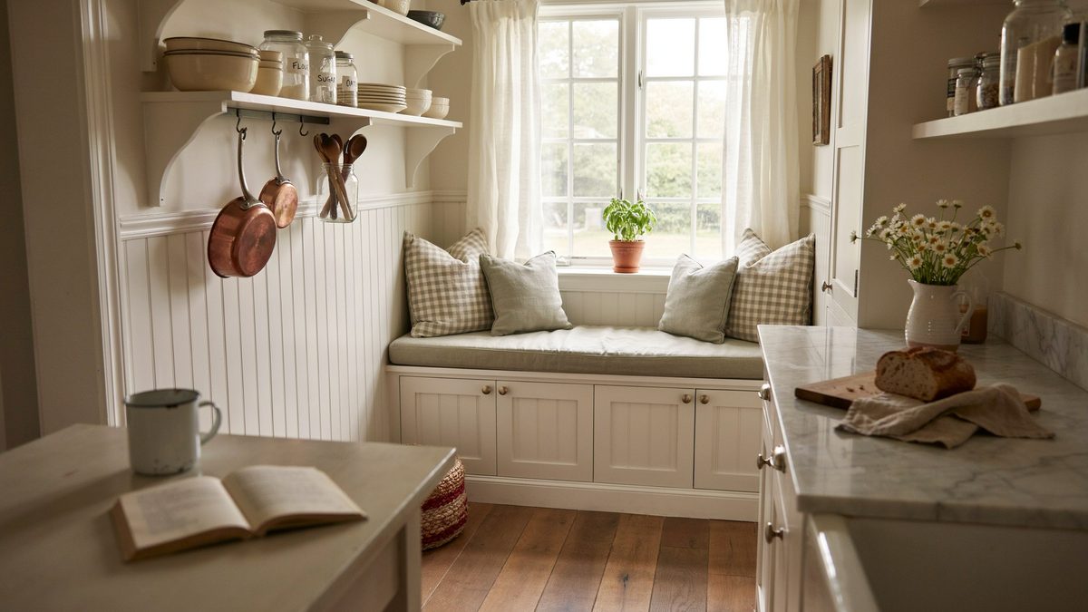 Cushioned window seat bench tucked between beadboard cabinets and a bright kitchen window