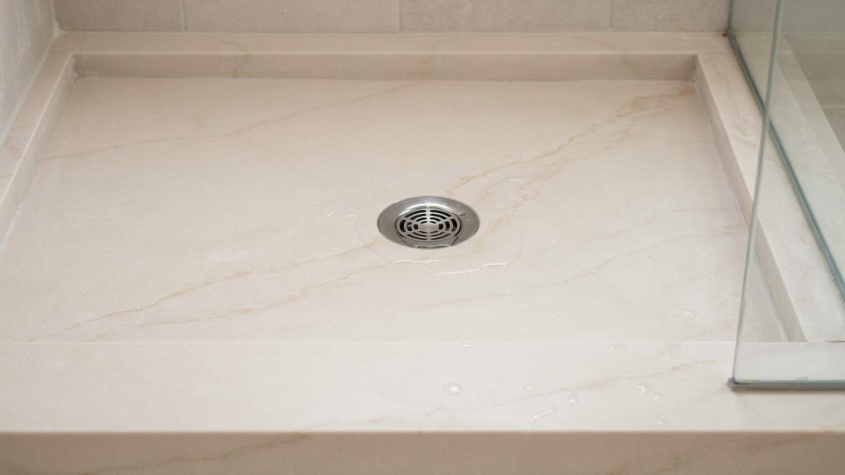 Cream cultured marble shower pan with low threshold curb and center chrome drain