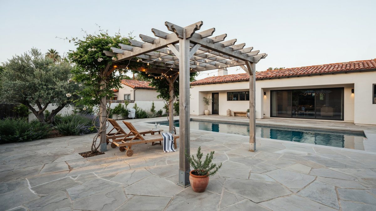 Weathered wood pergola with climbing vines beside a rectangular swimming pool