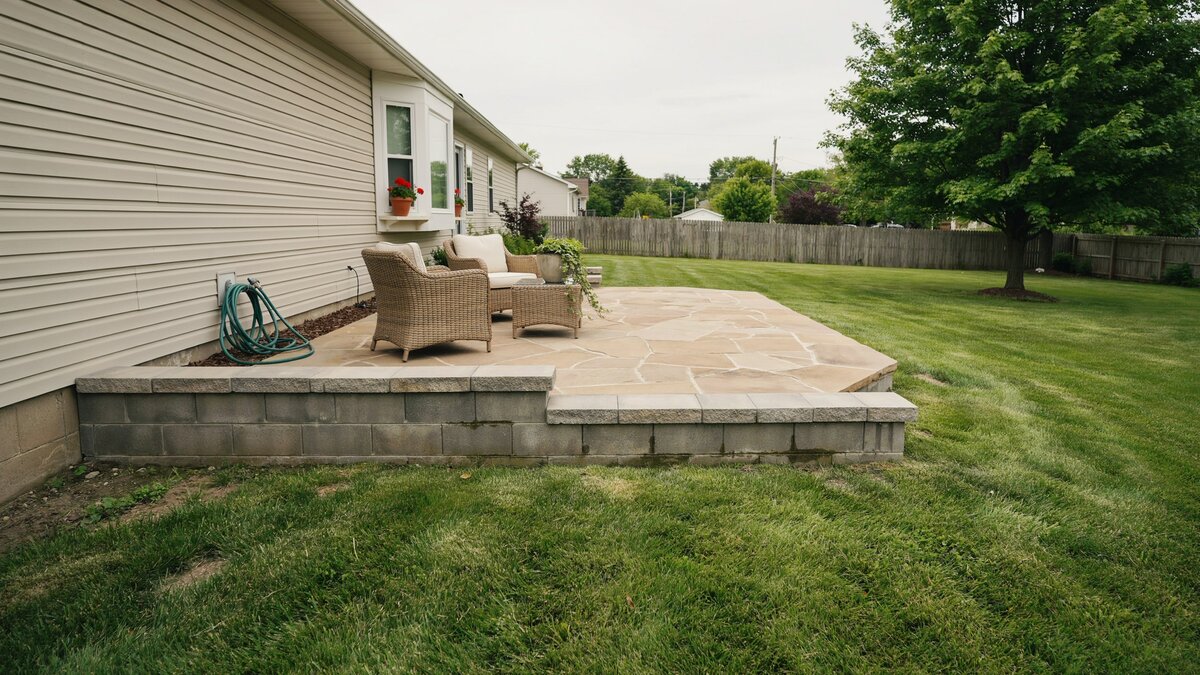 Raised tan stone patio held by a low gray concrete block retaining border
