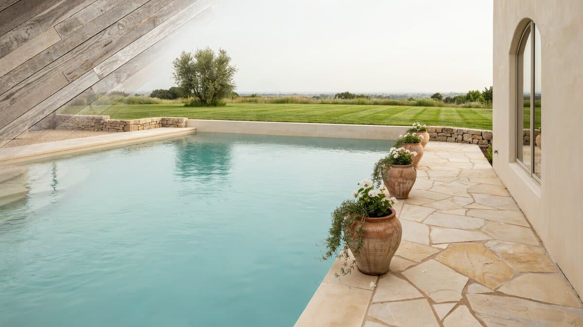 Beige stone pool surround edged in rough rock with terracotta planted urns