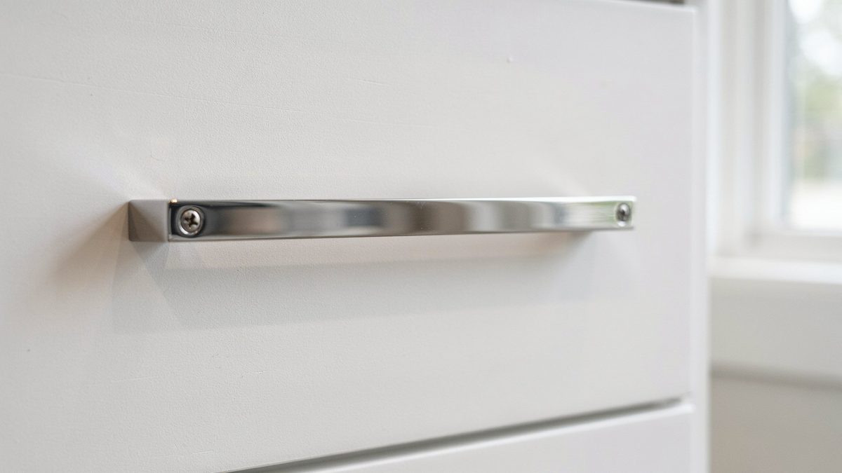 Slim chrome bar pull screwed across a white flat drawer front