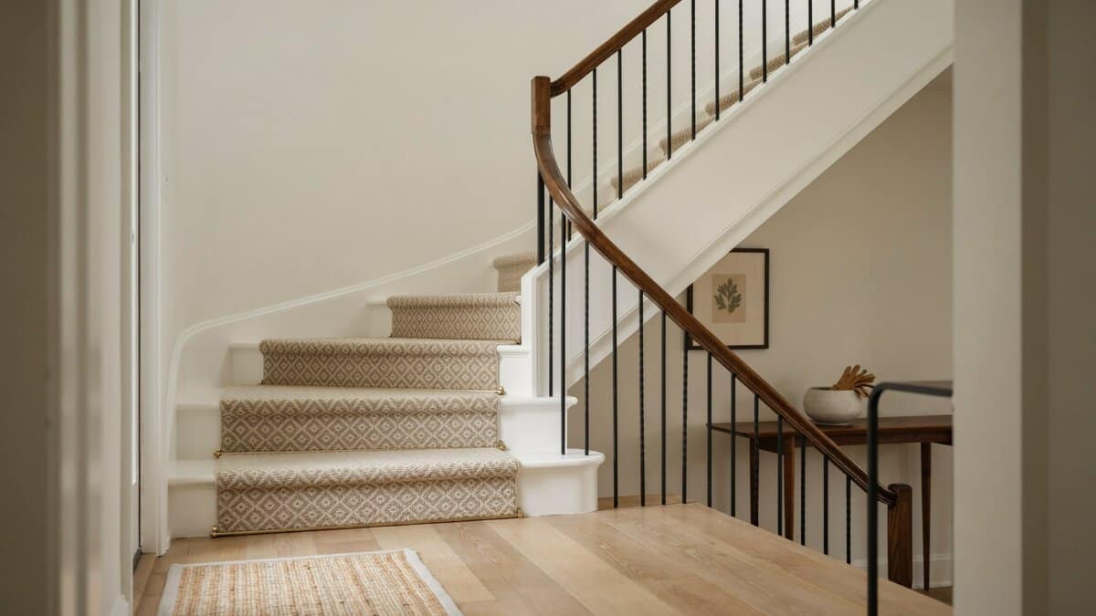 Carpeted staircase with patterned beige runner and dark wood handrail in a foyer