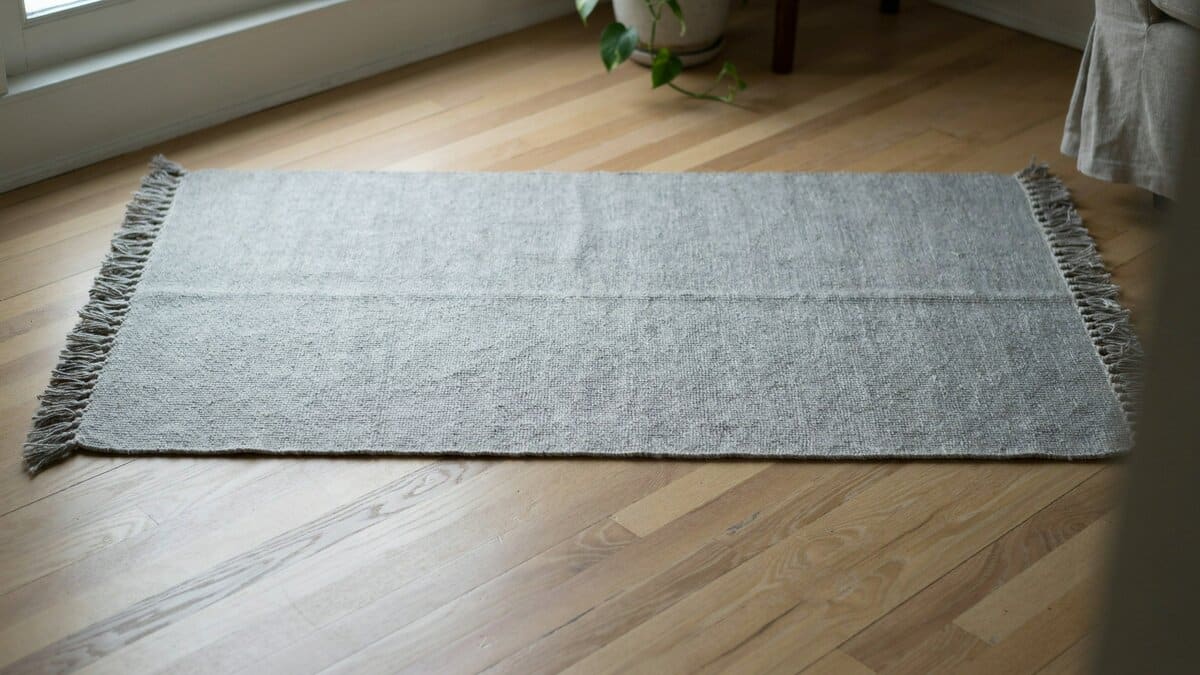 Gray flat woven cotton rug with fringed ends on pale wood flooring