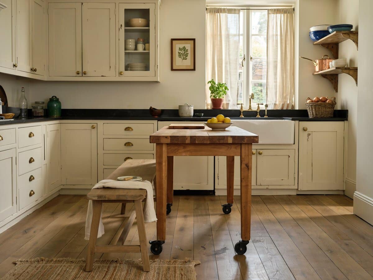 Cottage kitchen with antique white cabinets and a rustic wood island with dining bench