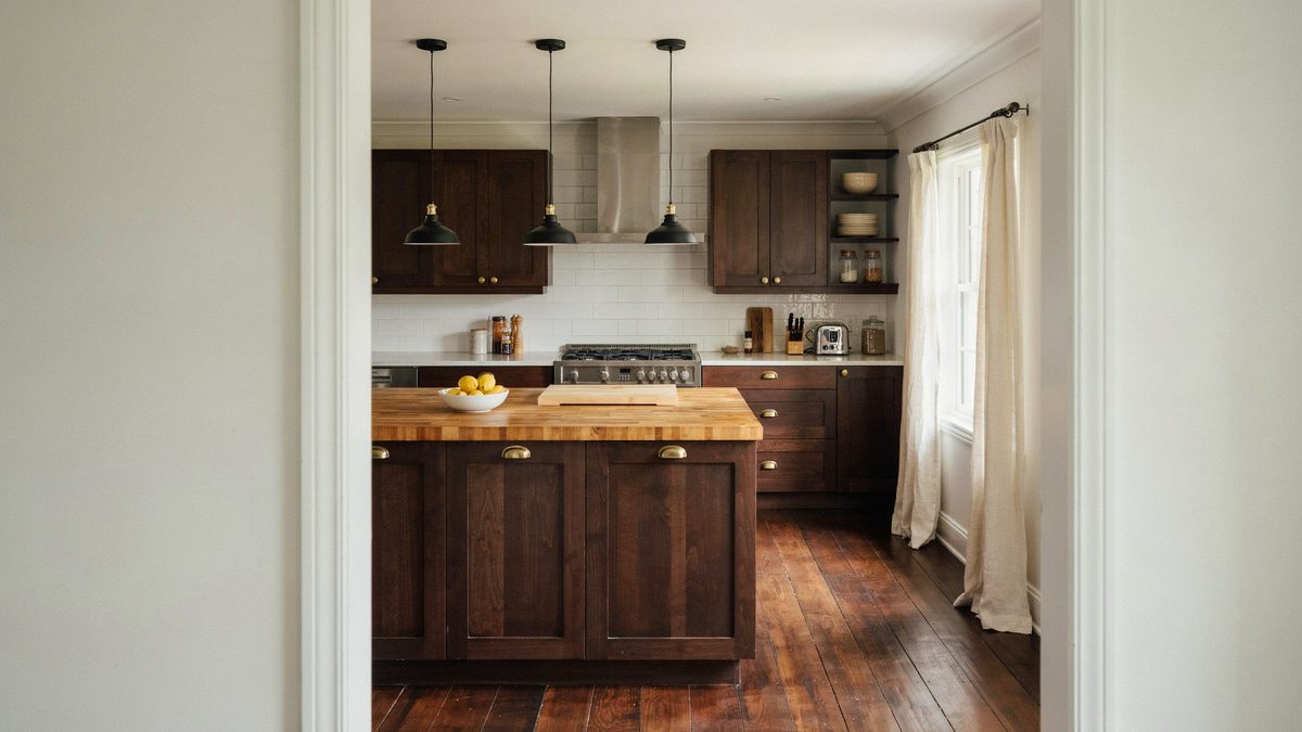 Dark wood kitchen with a butcher block island over stained teak floors